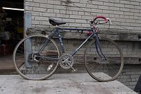Full side view of vintage Supercycle road bicycle showing frame, wheels, chain, pedals, and curved handlebar with pink grips.