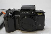 Front view of black Pentax SF1 35mm SLR camera with lens mount cap on and built-in pop-up flash showing Pentax branding.