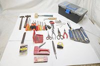 Full view of all hand tools and hardware items laid out on white surface with toolbox in background