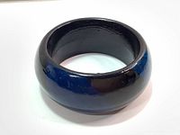 Front perspective of vintage chunky bangle bracelet showing glossy finish and broad rounded form in black and dark blue.