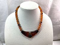 Front view of vintage amber-colored beaded necklace with large brown pendant on display bust.