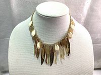 Front view of vintage women's fashion necklace displayed on a fabric bust showing dangling charms including cream-colored drops and gold-tone leaves.