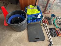View of orange hazard cones, safety vest, garden tubs and pots, kneeling pad, wheeled cart, gloves, and assorted hand tools.