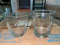 Side-by-side photo of one rounded and one fluted style clear glass cocktail glasses on cardboard box.
