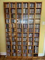 Three tall, narrow solid wood CD towers fully stocked with CDs, shown against a wall.