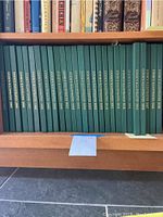 Photo showing a series of green hardcover cookbooks titled 'Cook's Illustrated' spanning from 1993 to 2019 arranged on a wooden shelf.