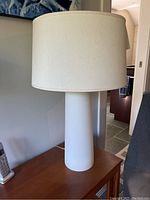 Front view of white cylindrical base lamp with off-white shade on a wooden table.