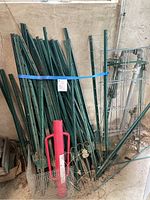 Bundle of green metal fencing/plant stakes of varying heights with blue strap and red stake driver in front.
