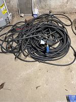 Three coiled heavy duty black rubber outdoor hoses on basement floor with visible hose ends and some attachments.