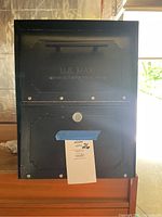 Front view of the black metal mailbox showing the locking door with secured keyhole and embossed text "U.S. MAIL Approved By The Postmaster General."