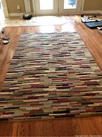 Image of full rug showing linear abstract pattern in multiple colors on hardwood floor.