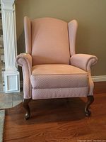 Front view of pink fabric wingback arm chair recliner with visible stains on the arm and seat upholstery, wooden cabriole legs.