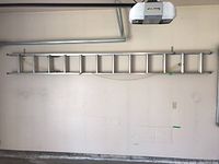 Full view of the aluminum extension ladder mounted horizontally on the wall showing length and condition.
