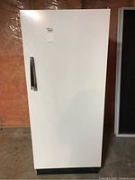 Front view of a white upright Admiral fridge with black handle, closed door, against unfinished wall.
