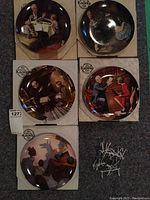 Photo showing 5 of the 6 Edwin M Knowles Norman Rockwell Grandfather Series plates in their original boxes, with assorted hanging wires in a separate pile.