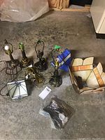 Photo showing four lamp bases, three stained glass shades, and a bag of light accessories on concrete floor