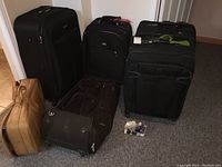 Six suitcases together showing variation in size, color, and wheels. Five are rolling upright suitcases, one is a smaller brown case without wheels.