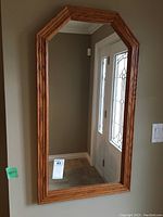 Full view of the wood-framed mirror mounted on a wall next to a door, showing the entire octagonal shape and reflection.