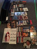 Photo showing an assortment of CDs, cassette tapes, DVDs, and two black metal music stands arranged on a carpeted floor.