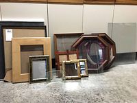 Various assorted picture frames including two large octagonal wooden frames, multiple rectangular frames, and glass panels on floor.