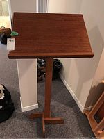 Front view of a tall solid wood podium with angled top and cross base.