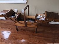 Full view of open retro wooden accordion sewing box on floor showing all compartments expanded.