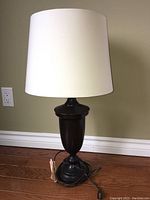 Full view of the black metal table lamp with white shade on hardwood floor against a beige wall.
