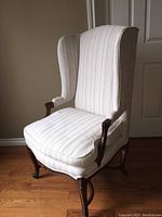 Full view of upholstered wing back arm chair with striped upholstery and dark wood legs on hardwood floor.