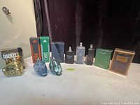 Wide view of all 11 cologne bottles and boxes arranged in a row on a table with black curtain background.