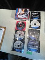 Stack of PS4 game cases with some discs outside the cases arranged on a white table.