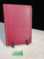 Red hardcover book with textured cover and embossed title on front, displaying overall aged condition.
