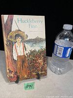 Front cover of vintage 1965 edition of Huckleberry Finn with illustration and water bottle for scale.