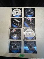 Photo showing 8 PS4 game discs in cases arranged in two columns and four rows on a white surface against black background.