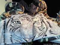 Photo showing a large sofa blanket with a tiger face design in muted colors, slightly wrinkled but overall in good shape.