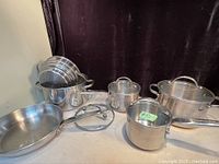 Front view showing stainless steel pots and pans with handles and lids on a white surface against black backdrop