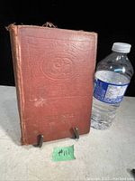 Front cover of the antique book showing reddish-brown cover with embossed design and visible wear.