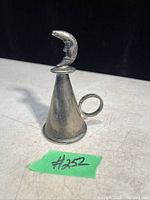 Photo of vintage metal candle snuffer featuring a crescent moon face on the handle, positioned against a neutral background to show size and details.
