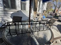Single solid iron flower pot holder placed on glass table outdoors, showing curved iron bars and mounting brackets.