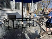 Photo of a solid iron flower pot holder with scrollwork on a glass patio table, showing the full item and its structure.
