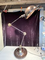 Full view of large articulated lamp showing black base, brass arm joints, and large metal shade
