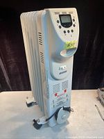 Front view of Garrison white oil-filled radiator space heater showing the digital display, control buttons, handle, power cord wrapped on the base, and caster wheels (one missing a nut).