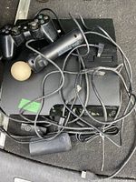 PS3 controller, PlayStation Move controller with white ball, power cord, and cables on top of PS3 console