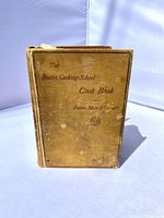 Front cover of the 1925 Boston Cooking School Cookbook by Fannie Merritt Farmer, showing brown cloth cover with black printed title and visible wear spots and stains.