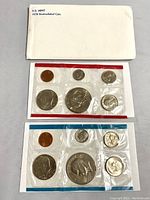 Photo of two sets of uncirculated 1978 US Mint coins sealed in plastic, one with red border and one with blue border, including envelope.