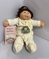 Front and slightly side view of the doll standing with birth certificate and adoption papers