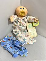 Front view of Cabbage Patch preemie baby doll wearing gown and pacifier, showing original tag and original clothing along with small blue blanket.