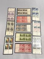 Top view of 11 blocks of US stamps showing a variety of colors, designs, and denominations, each block containing connected stamps individually packaged.