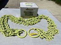 Full view of green BrushGrubber metal chain with two large metal rings, laid out on a grid table next to the product box.