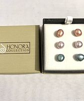 Overview of the Honora Collection branded beige box alongside the opened black and white cushioned box showing three pairs of freshwater cultured pearl post earrings in pink, blush, and pale blue.