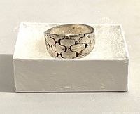 Front and angled view of the silver ring on white box showing the textured interlocking geometric pattern on the band.